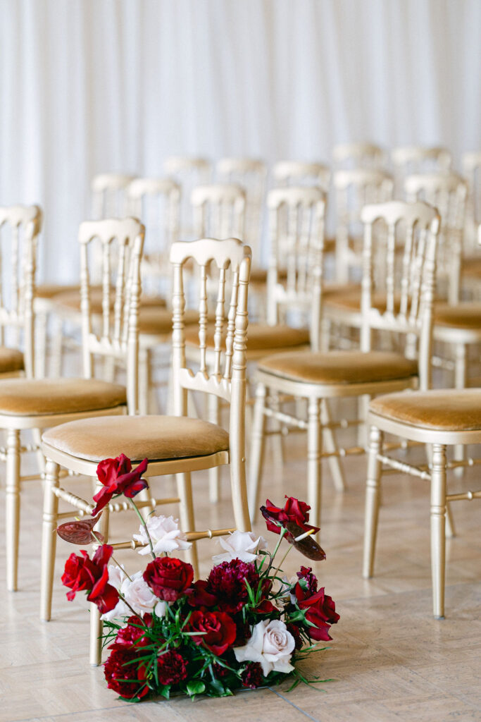 Gold Chiavari chairs arranged in rows for a wedding ceremony at Cercle Cité Luxembourg with a deep red and blush floral arrangement lining the aisle