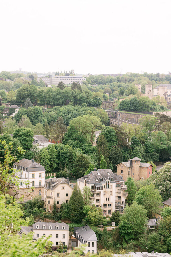 Aerial view of the Grund neighborhood in Luxembourg City with lush greenery, historic stone buildings, and fortress walls