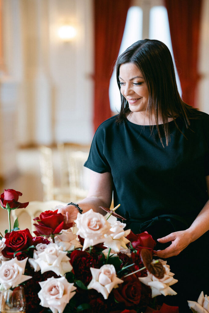 Luxembourg wedding planner Lynn arranging deep red and blush rose centerpieces inside Cercle Cité on the morning of a wedding