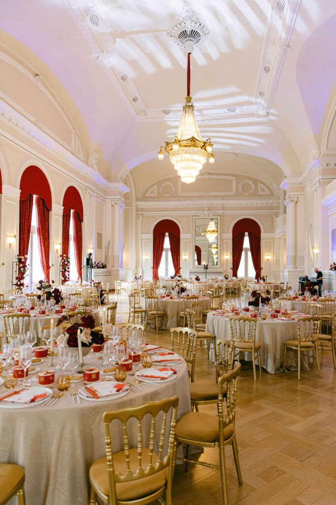 Wide view of the fully decorated wedding reception hall at Cercle Cité Luxembourg with round tables, gold Chiavari chairs, and crystal chandeliers