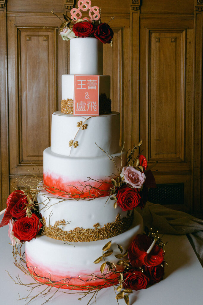 Four-tier wedding cake with red ombre brushwork, gold leaf details, deep red roses, and Chinese character monogram topper by Chocolate House Luxembourg