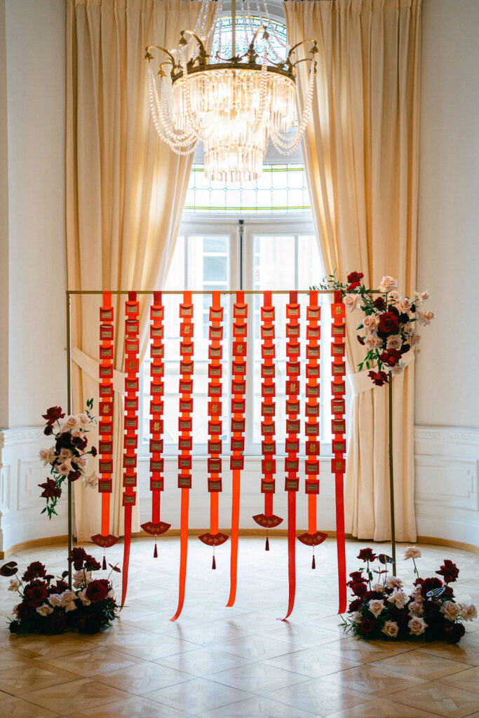 Modern wedding ceremony backdrop at Cercle Cité featuring a geometric red ribbon installation, chandelier, and deep red floral accents