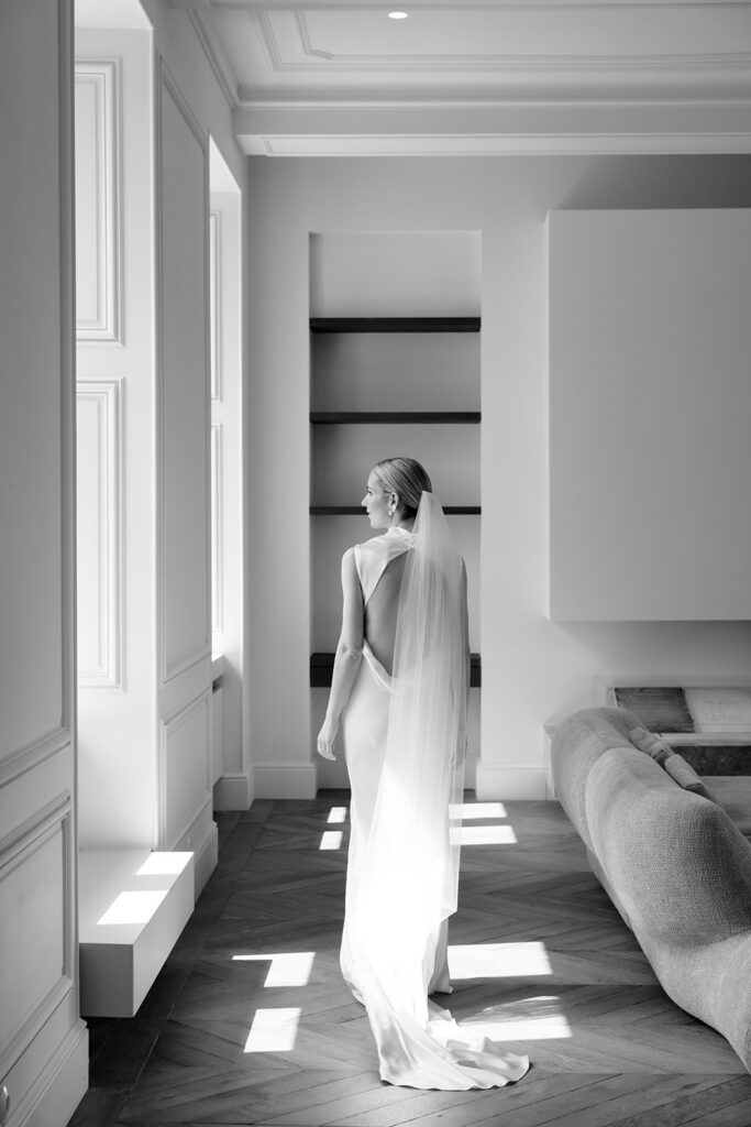 Black and white bridal portrait of Carla in open back silk gown standing in light filled room at Château de Mirwart Belgium