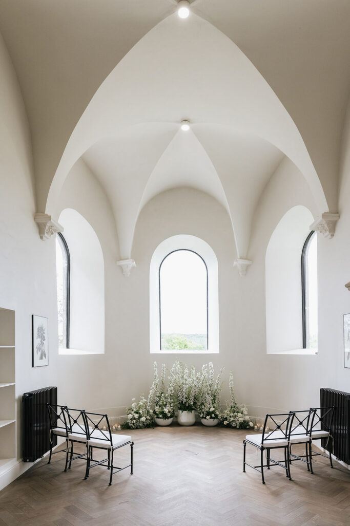 Intimate wedding ceremony chapel interior at Château de Mirwart Belgium with white gothic arched ceiling natural light and simple floral arrangements