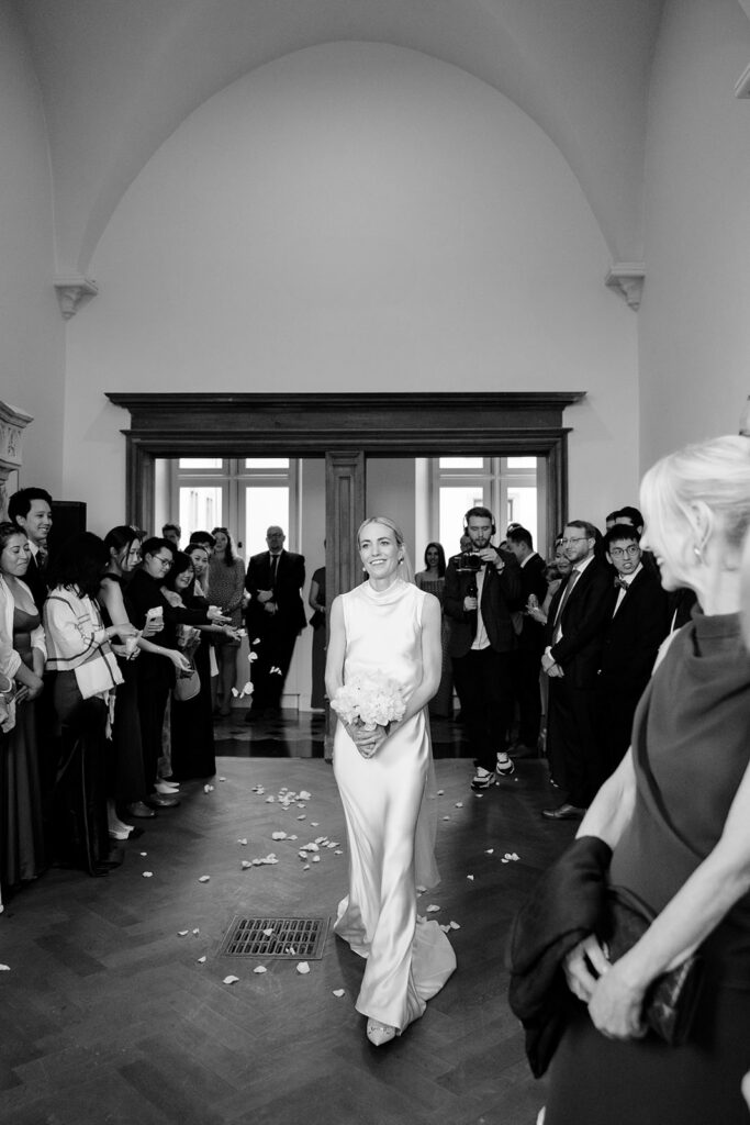 Bride Carla walking down the aisle in her minimalist silk gown at her intimate wedding ceremony inside Château de Mirwart Belgium black and white