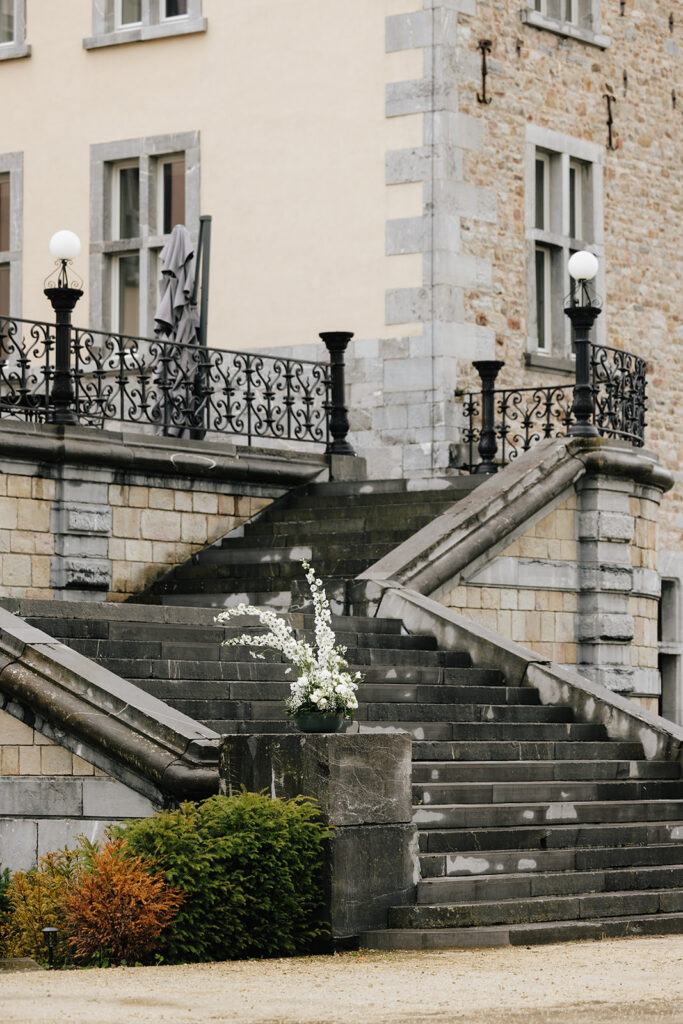 Château de Mirwart exterior stone staircase with wrought iron railing and white floral arrangement Belgium wedding venue