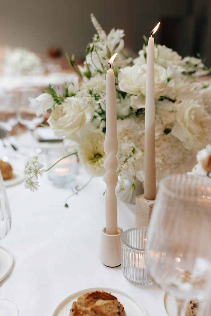Wedding reception table detail at Château de Mirwart Belgium with white floral centerpiece by Catherine Alves taupe taper candles and ribbed glassware