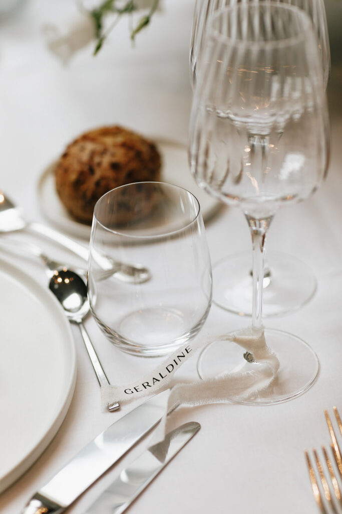 Close up of hand lettered wedding place card and crystal glassware on a reception table at Château de Mirwart Belgium