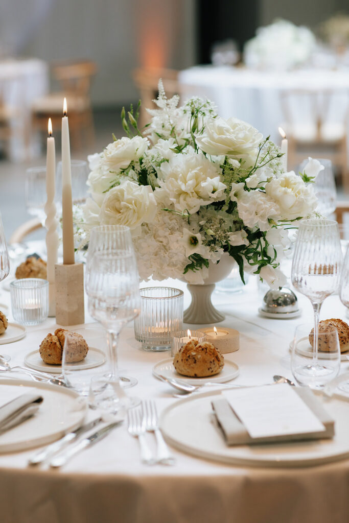 Wedding reception table setting at Château de Mirwart Belgium with white hydrangea centerpiece taupe candles ribbed glassware and elegantly folded napkins