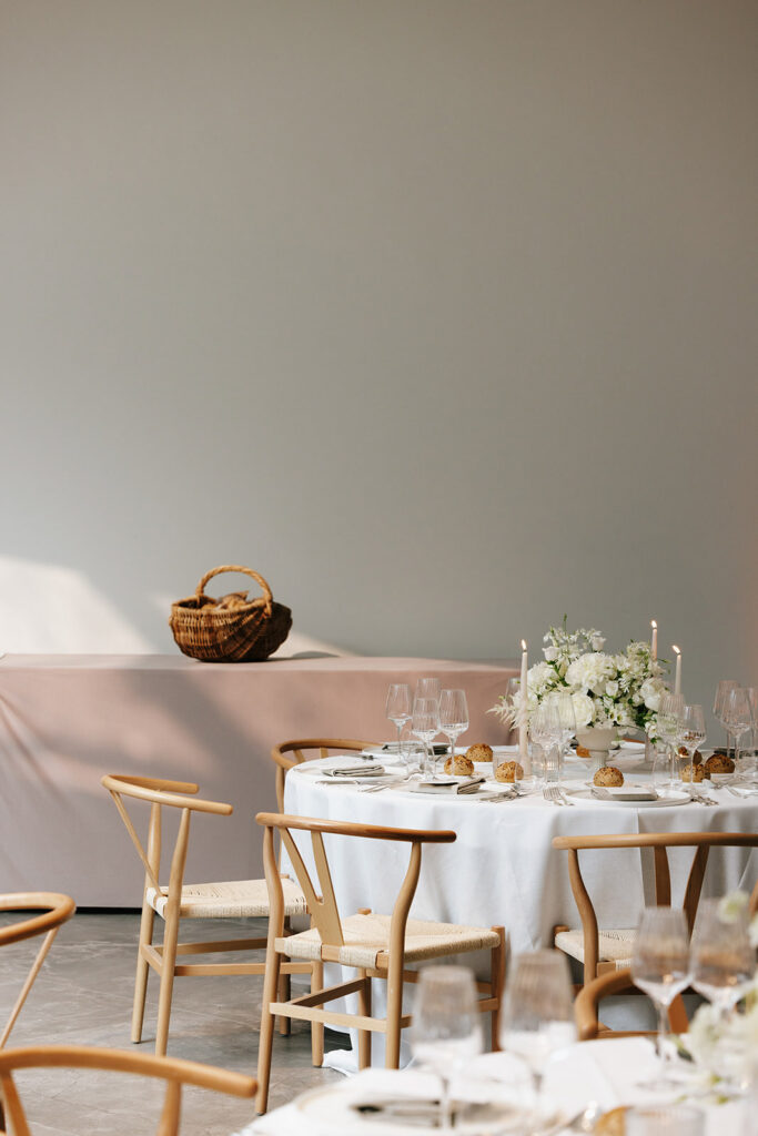 Wide view of wedding reception room at Château de Mirwart Belgium with round tables wishbone chairs white florals and soft candlelight