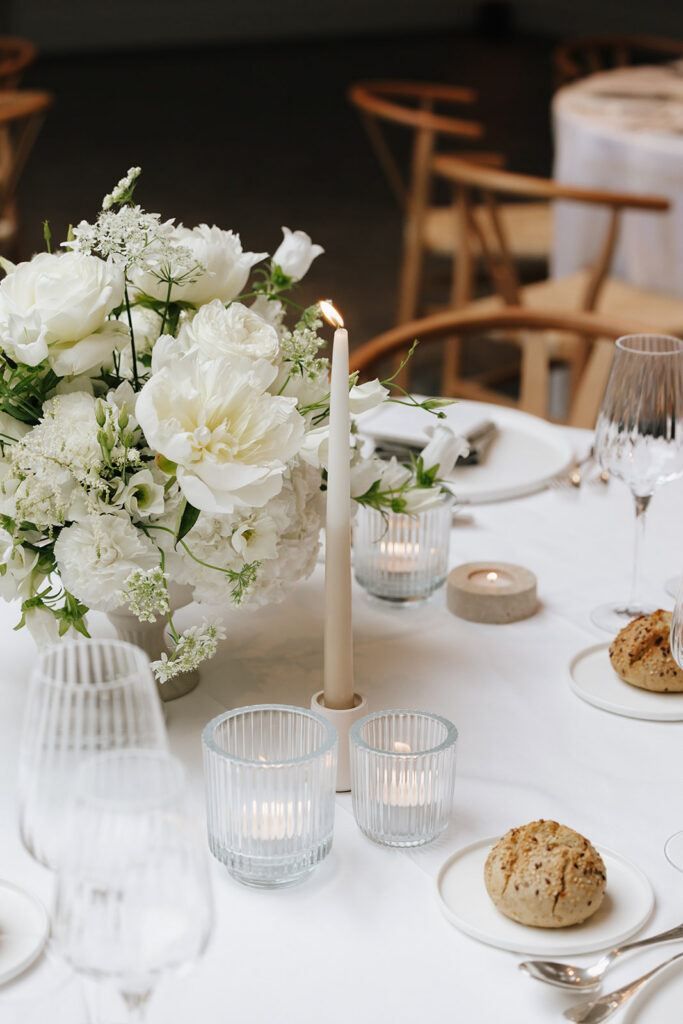 Close up of white peony and hydrangea floral centerpiece by Catherine Alves with taupe taper candle and votive candles at Château de Mirwart wedding reception