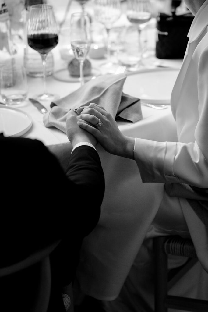 Black and white close up of bride and groom holding hands at the wedding reception table at Château de Mirwart Belgium