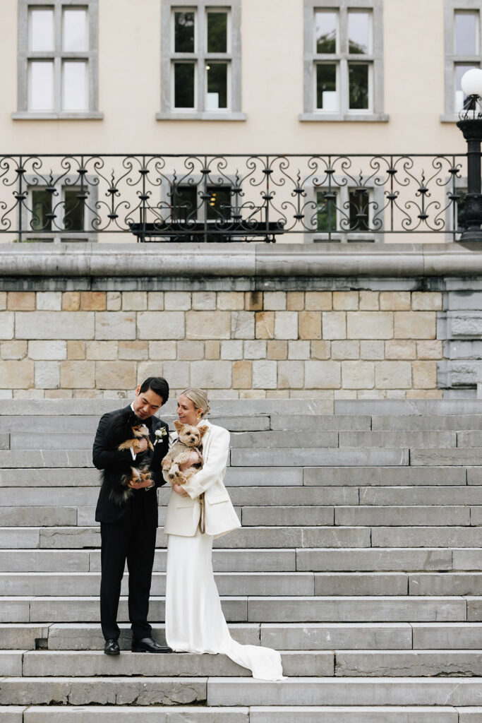 Carla and Robin holding their two dogs on the stone steps of Château de Mirwart Belgium in their wedding attire