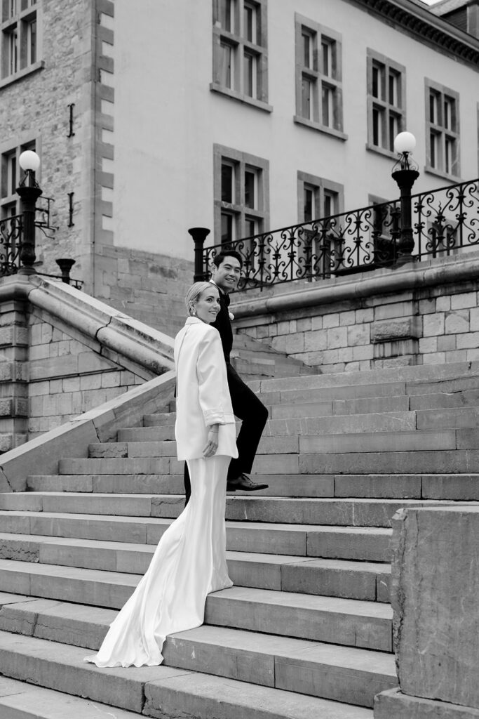 Carla and Robin wedding portrait on the stone steps of Château de Mirwart Belgium bride wearing a white bridal coat over her gown with groom in black suit