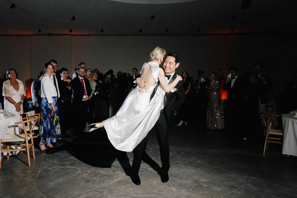 Robin lifting Carla during their first dance at the wedding reception at Château de Mirwart Belgium with guests watching and cheering around them