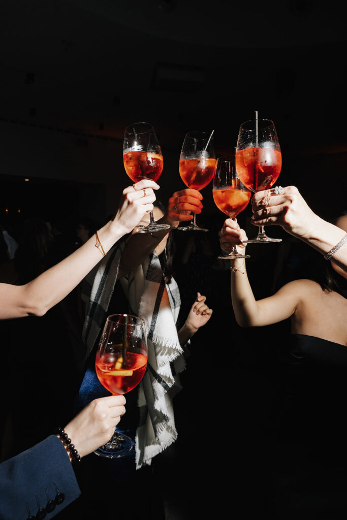 Wedding guests raising Aperol Spritz glasses in a toast at the Château de Mirwart wedding reception in Belgium