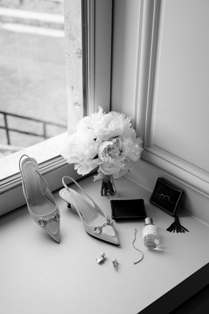 Bridal details flat lay at Château de Mirwart wedding including heels bouquet jewelry and perfume on a window ledge