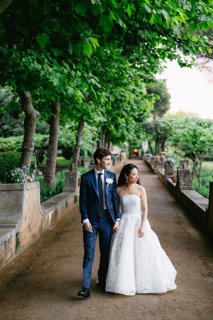 Crystal and Cobi walking hand in hand through the tree lined garden path at Villa Cimbrone Ravello Italy after their wedding ceremony
