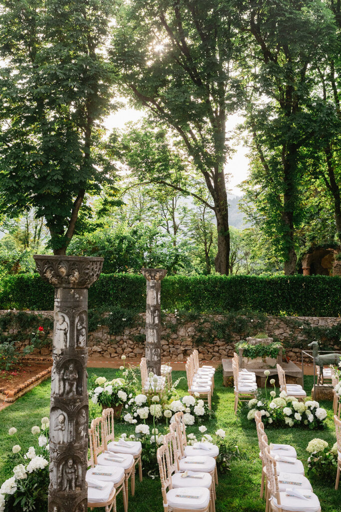 Outdoor wedding ceremony aisle at Villa Cimbrone Ravello lined with white floral arrangements and guest seating surrounded by Italian cypress and garden hedges