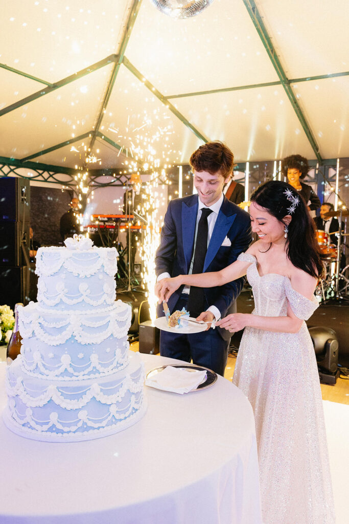 rystal and Cobi cutting their pale blue tiered wedding cake with sparklers exploding behind them and a live band performing at their Villa Cimbrone reception in Ravello Italy