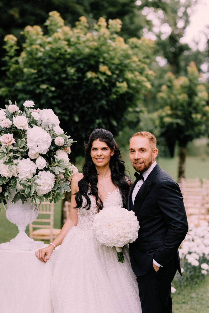 Bride and groom wedding portrait beside a large white floral urn arrangement by Claudia Leinen on the grounds of Château du Bois d'Arlon Belgium