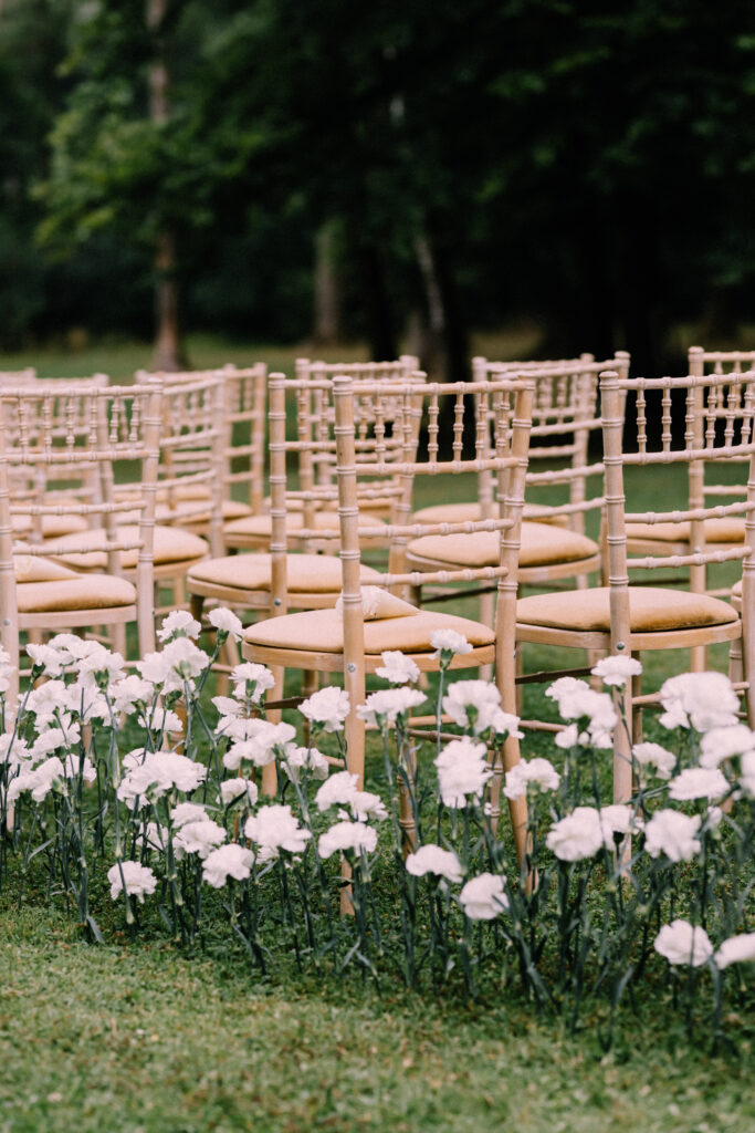 Gold Chiavari chairs arranged for an outdoor wedding ceremony at Château du Bois d'Arlon Belgium with white carnations lining the lawn