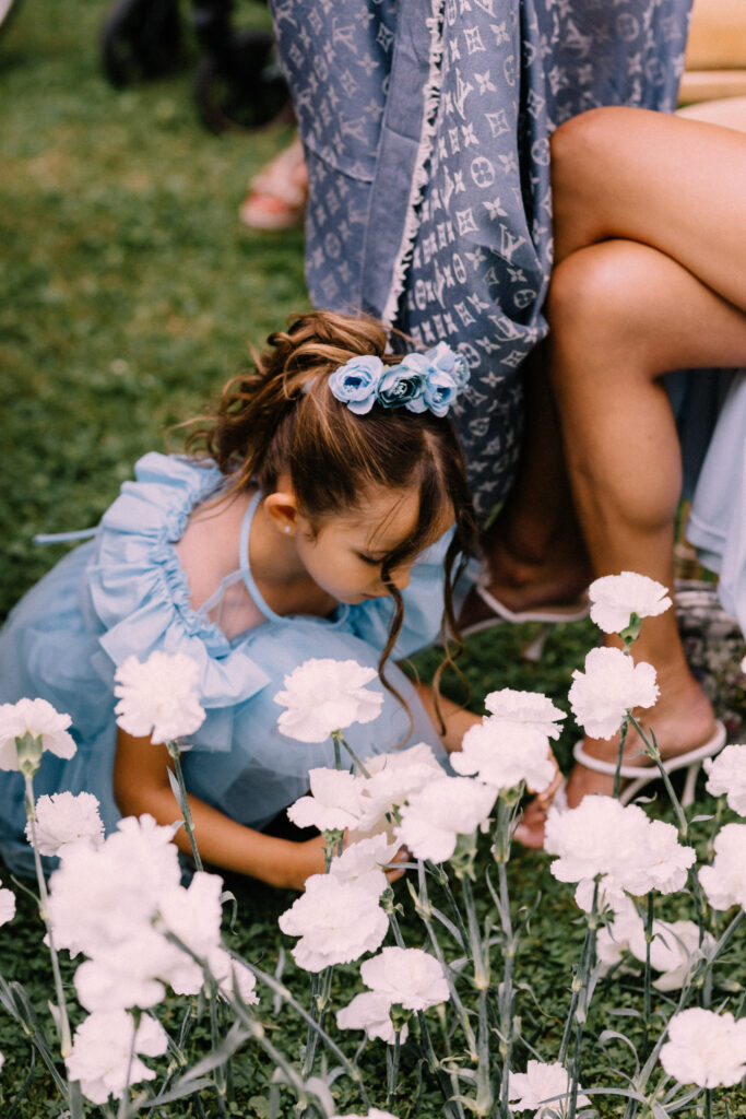 Young flower girl in blue dress picking white carnations from the ceremony lawn at Château du Bois d'Arlon Belgium