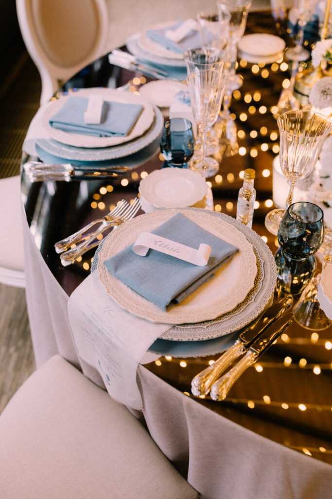 Close up of wedding reception place setting at Château du Bois d'Arlon Belgium with blue linen napkin white china gold cutlery and crystal glassware