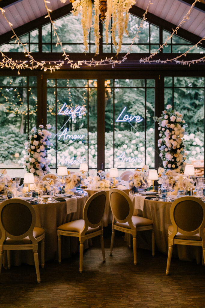 Wedding reception room at Château du Bois d'Arlon Belgium with neon love signs in multiple languages Louis XVI chairs blush floral arrangements and fairy light ceiling