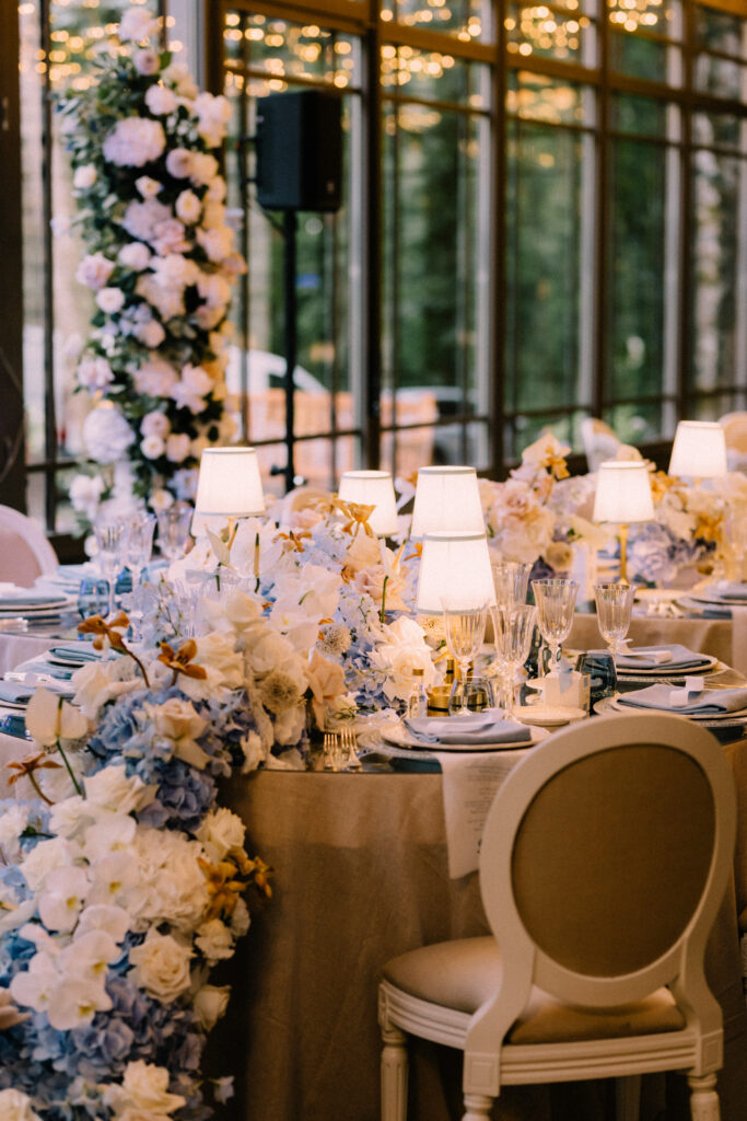 Wedding reception table with blue and white hydrangea floral runner Louis XVI chairs and table lamps at Château du Bois d'Arlon Belgium