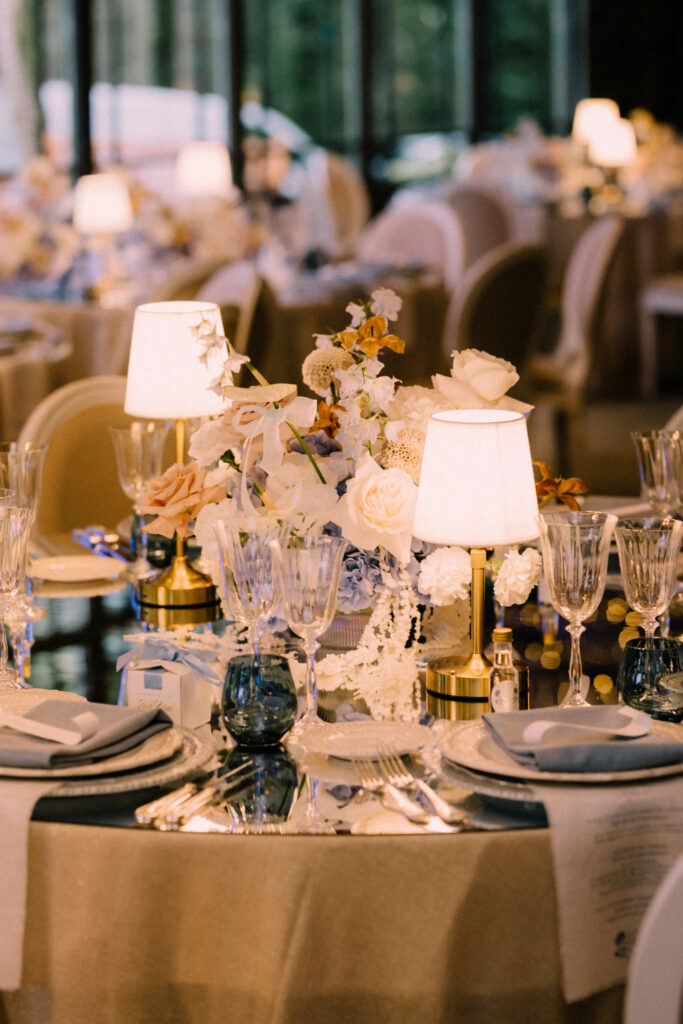 Wedding reception table detail at Château du Bois d'Arlon Belgium with mirror top table design by Luxwedding blush florals table lamps and blue glassware