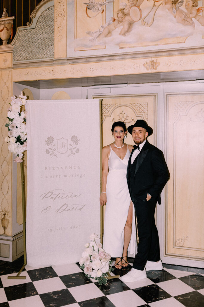 Bride and groom posing at the custom wedding photo booth with branded welcome sign and floral arrangement at Château du Bois d'Arlon Belgium