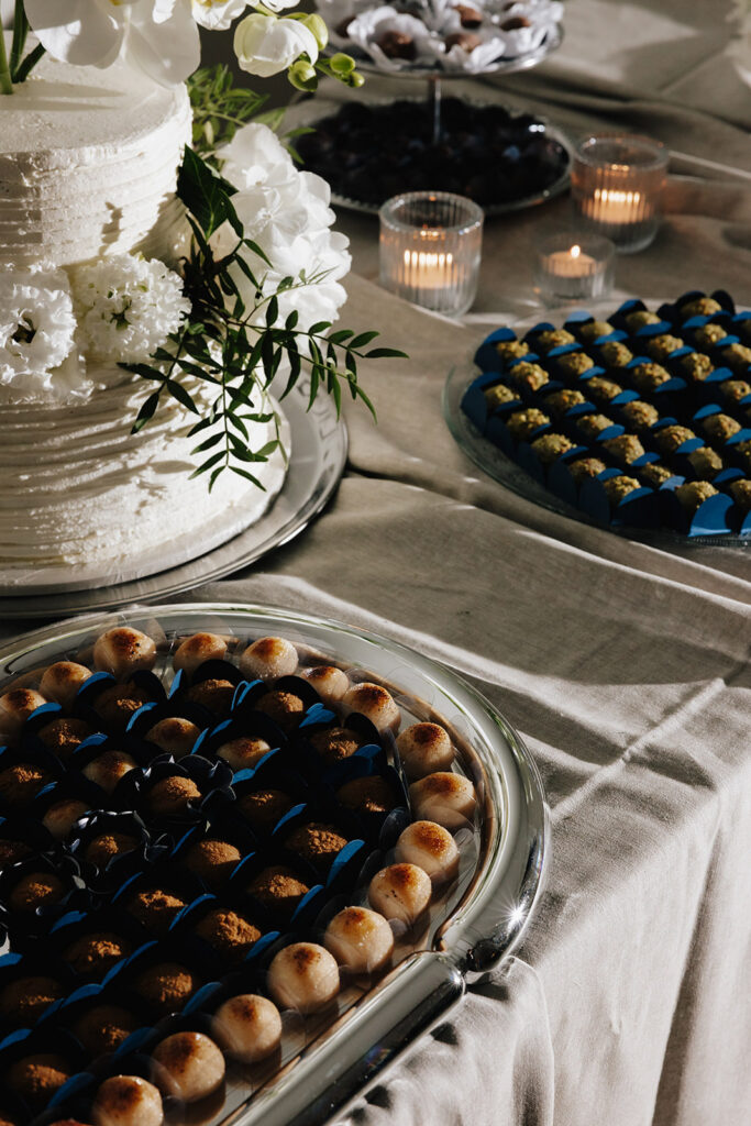 Hazelnut House 1851 Luxembourg wedding dessert detail, a white tiered cake trimmed with fresh florals beside trays of blue and gold wedding sweets