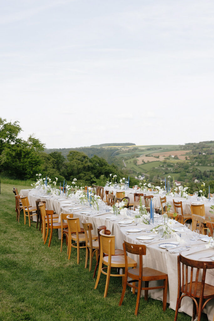 Hazelnut House 1851 Luxembourg wedding banquet tables set with wooden chairs and airy white florals, the countryside and open sky stretching behind